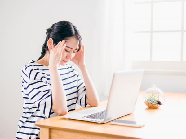 家でパソコン操作している頭痛の女性